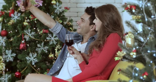 Young Caucasian Couple sitting on sofa, they selfie teir photo by man cellphone, have a glasses wine in their hands to celebrated special time, concept for Christmas festival. photo