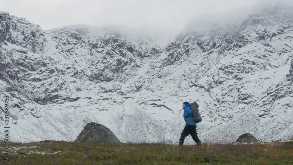 A man with a backpack, alone, traveling in the mountains. It goes along high snowy peaks. A man with a backpack, alone, traveling in the mountains. It goes along high snowy peaks.