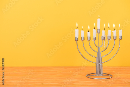 close up view of menorah with candles for hannukah holiday celebration on wooden tabletop isolated on yellow, hannukah concept