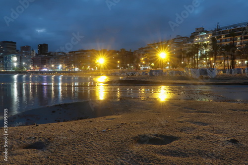 Deserted sunset beach at sunset in Benidorm, Spain, with the reflection in the water of the lights of the buildings on a cloudy day with the hammocks stacked in the sand
