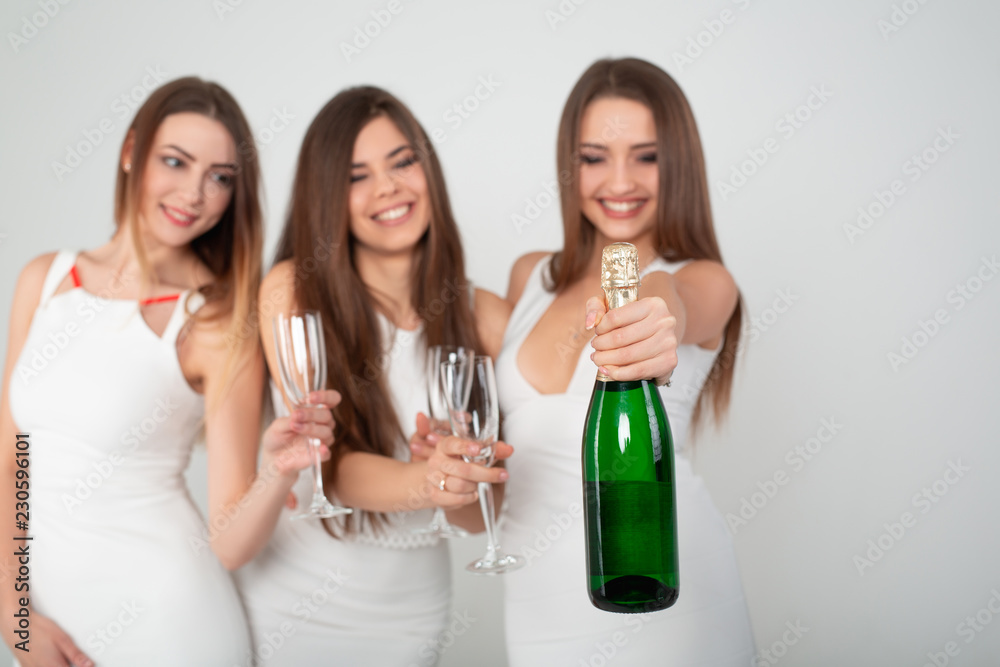 Three young woman in elegant dresses having fun, smiling, dancing and drinking champagne in studio on white background. Christmas party celebration concept. Three young woman in elegant dresses having fun, smiling, dancing and drinking champagne in studio on white background. Christmas party celebration concept.