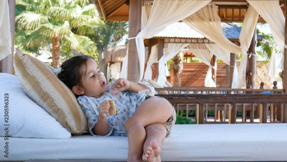 The little cute girl is resting, talking and eating on the soft seats of the gazebo.