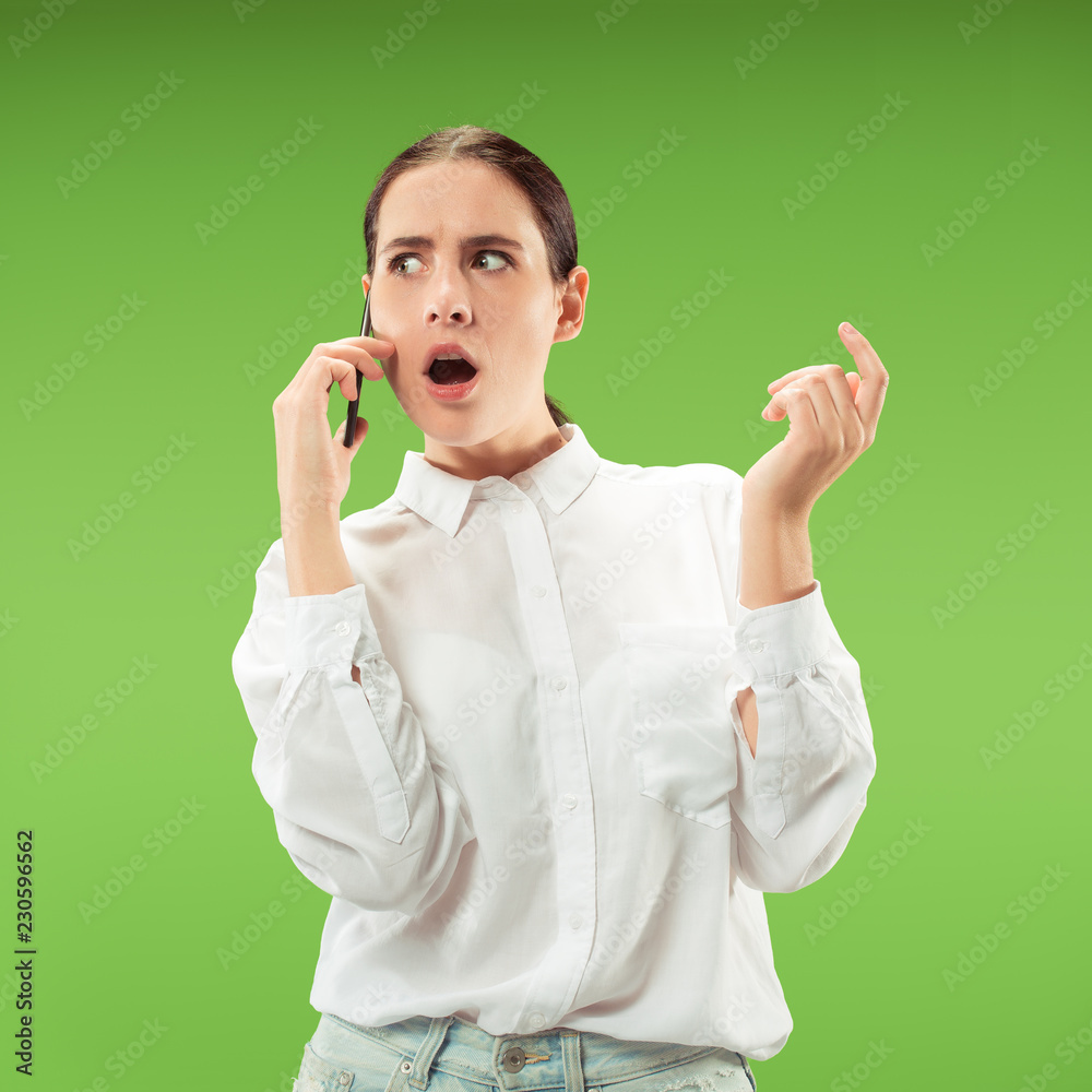 Young beautiful woman using mobile phone studio on green color studio background. Human facial emotions concept. Trendy colors