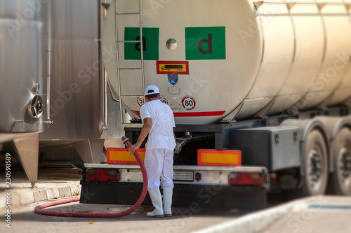 Male worker loading truck container with milk in an industrial cheese production factory