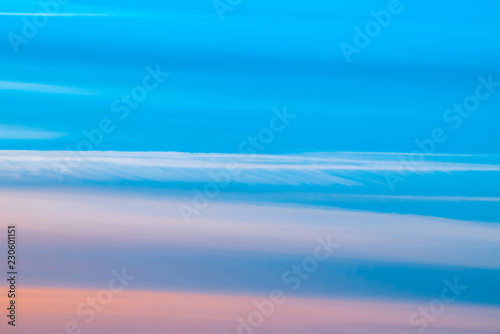 Varicolored striped surreal sky with shades of blue, cyan, cobalt, pink colors. Horizontal lines of smooth clouds. Atmospheric background image of tender sky.