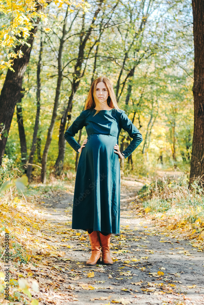 Beautiful portrait of pregnant woman belly in a warm dress in colorful autumn forest in September. The concept of pregnancy and the seasons