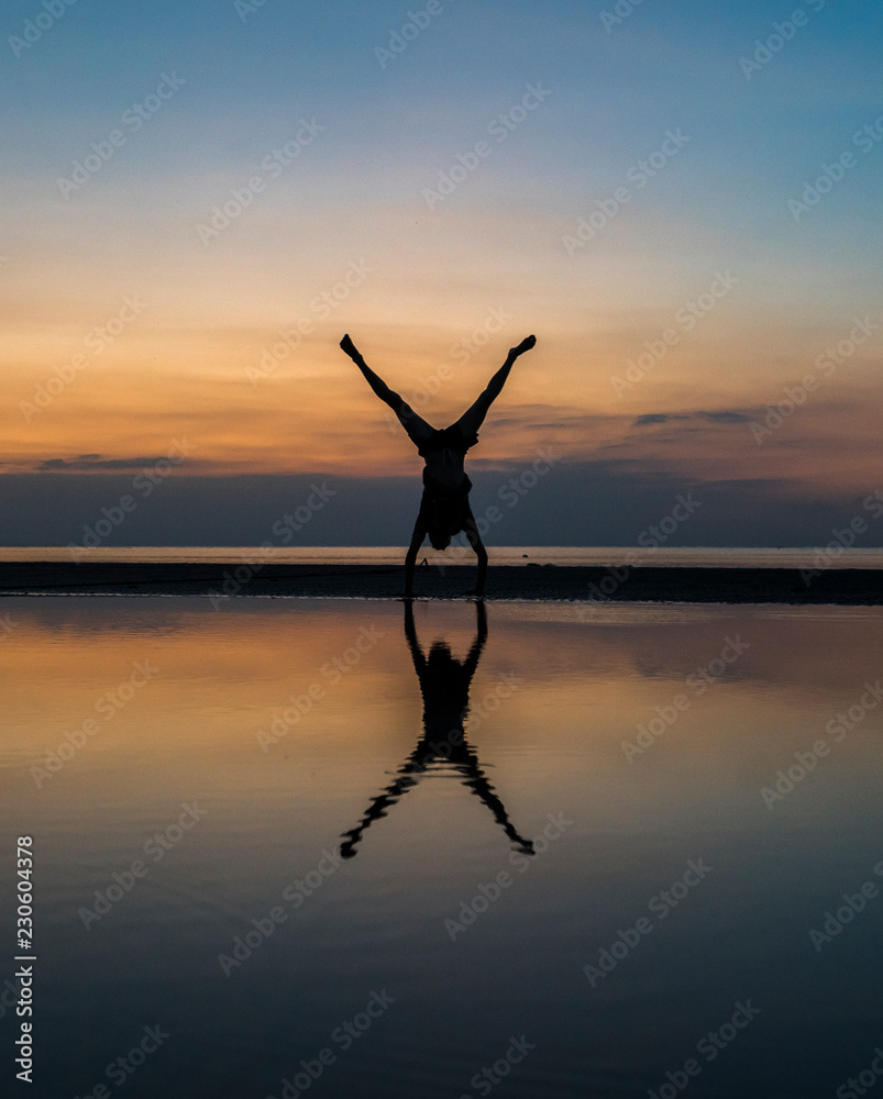 Young man performing a handstand on the water during sunset (beautiful reflection)