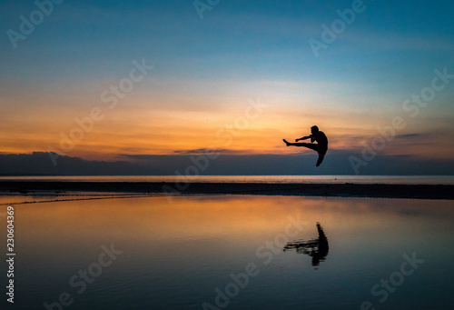 young athletic guy performing a flying kick during sunset on the beach © rene gamper