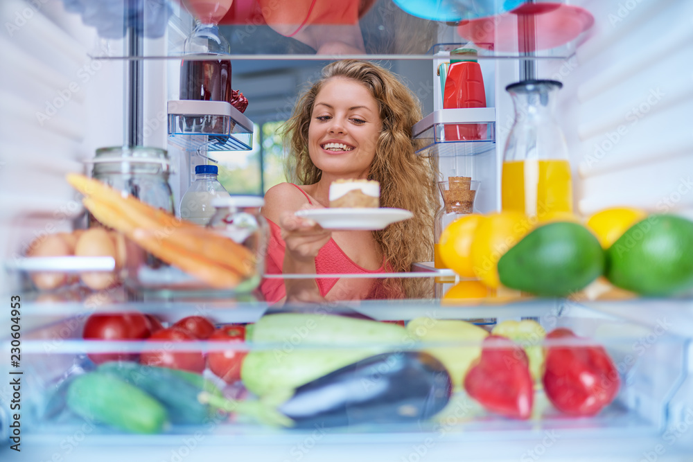 Woman taking gateau form fridge full of groceries. Unhealthy eating concept. Picture taken from the inside of fridge. Woman taking gateau form fridge full of groceries. Unhealthy eating concept. Picture taken from the inside of fridge.