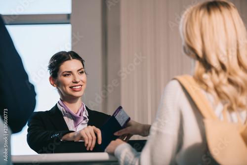 cropped shot of airport worker giving passport with boarding pass to young woman at check-in desk