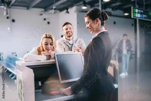 Fotografie smiling young travelers at check-in desk in airport