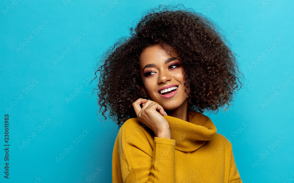 Beautiful smiling african american woman with an afro hairstyle looking on empty space isolated on blue background Beautiful smiling african american woman with an afro hairstyle looking on empty space isolated on blue background