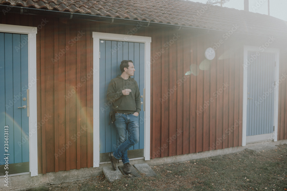 Mann raucht Zigarette vor einem Blockhaus in Schweden
