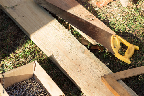 box of nails, boards, hand saw lying on the grass