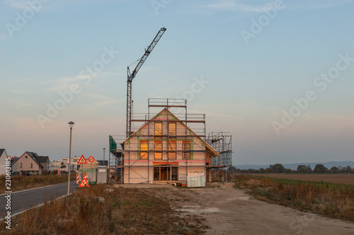 Eingerüsteter Rohbau mit eingebauten Fenstern und Kran im Hintergrund beleuchtet von der rötlichen Abendsonne