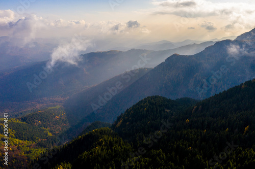 Aerial photography over big mountain forest. Sunset over the forest. Foggy valley at the sunrise. Golden hour over the forest with mist. Beautiful aerial landscape. Drone shots over the foggy forest. 