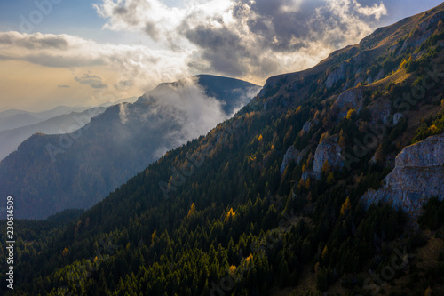 Aerial photography over big mountain forest. Sunset over the forest. Foggy valley at the sunrise. Golden hour over the forest with mist. Beautiful aerial landscape. Drone shots over the foggy forest. 