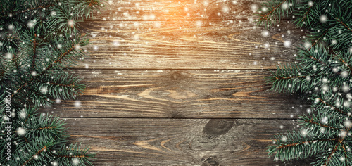 Old wood background with fir branches. Space for a greeting message. Christmas card. Top view. Effect of light and snowflakes.