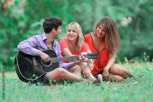 group of students with a guitar relax sitting on the grass in the city Park © yurolaitsalbert