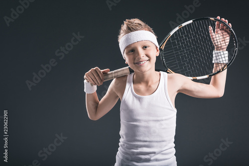 portrait of cheerful boy in sportswear with tennis racket on dark background © LIGHTFIELD STUDIOS