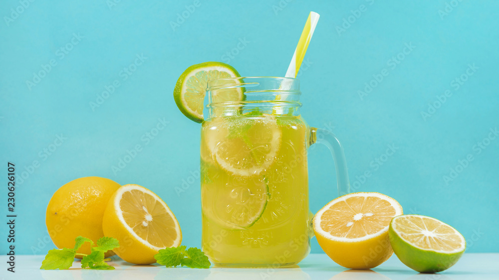 Lemonade drink of soda water, citrus and mint on the light blue background. Cocktail glass with handle and straw, sliced lemon and lime, front view Lemonade drink of soda water, citrus and mint on the light blue background. Cocktail glass with handle and straw, sliced lemon and lime, front view