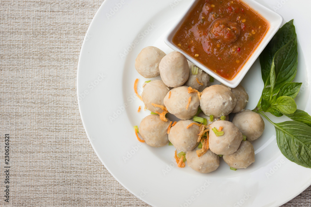 Boiled pork balls with sweet spicy sauce in white plate on gray table mat; top view Boiled pork balls with sweet spicy sauce in white plate on gray table mat; top view