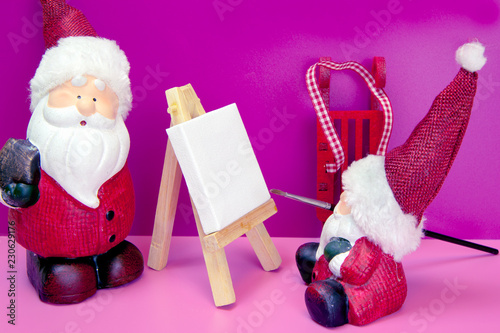 Cute small Santa Claus is painting a bigger Santa Claus on the artistic canvas with brush. Christmas and New Year holiday background concept. Copy space for text.