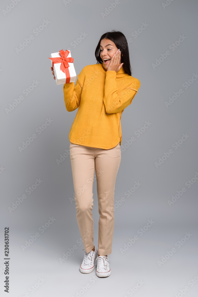Excited woman posing isolated over grey wall background holding box surprise present. Excited woman posing isolated over grey wall background holding box surprise present.