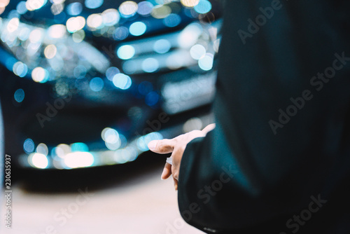 Unidentified business man on car showroom and cars blurry background. Handsome elegant man in suit, businessman or salesman, stretches his hand to conclude a business with contract/ notebook in hands