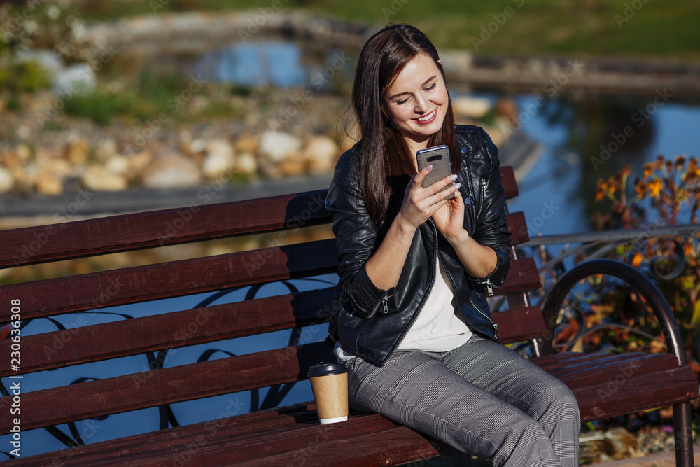 Smiling caucasian woman with smartphone sitting in park Smiling caucasian woman with smartphone sitting in park
