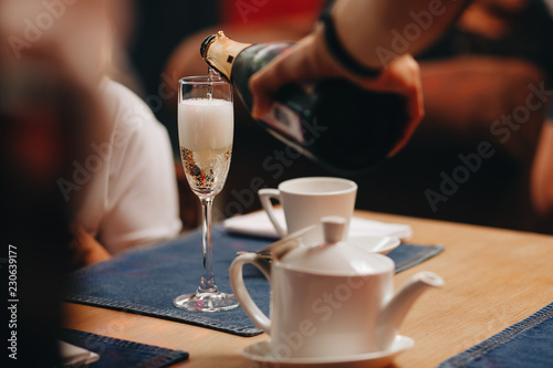 Photos Sommelier pours champagne from a bottle into a glass at the table in the restaurant