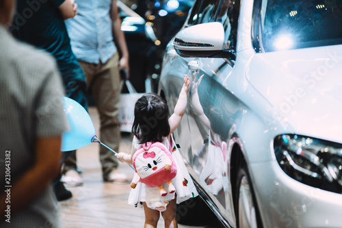 Unidentified Asian baby girl touching car door handles. Never leave a baby sitting alone in car front seat without a baby car seat and its safety belt fastened © Dung