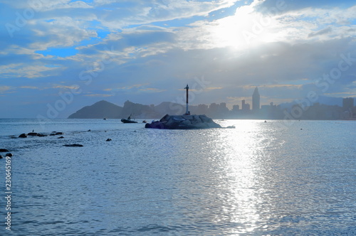 Mediterranean sea in Benidorm, Spain, with a view to the bottom of the buildings of the west beach. Cloudy sunset with the sun rising through the clouds and reflecting in the water of the ocean. 