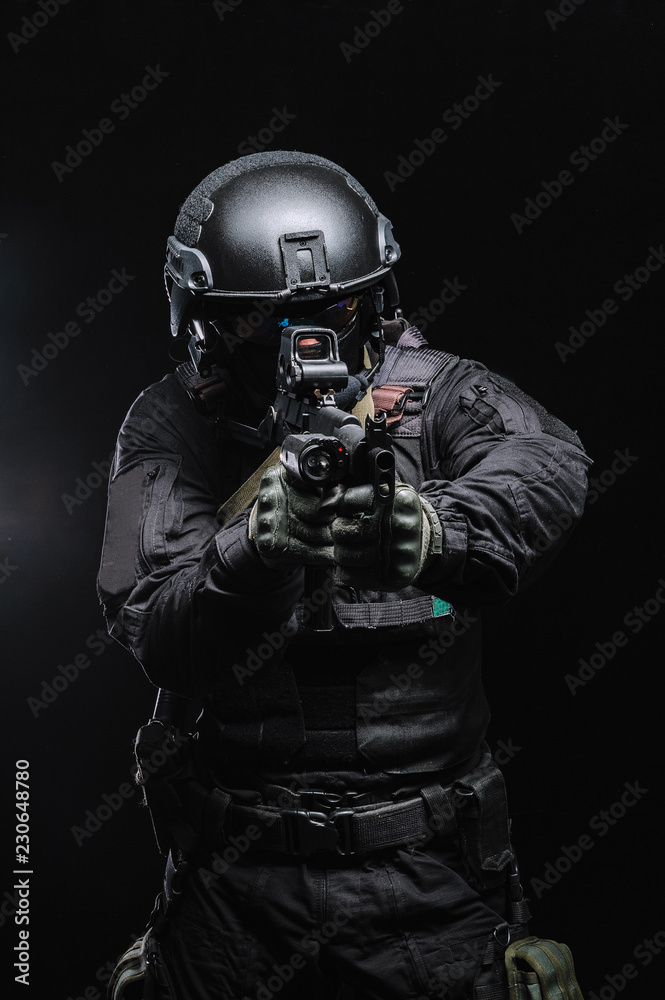 Military man in combat gear with weapons on a black background. Vertical frame.