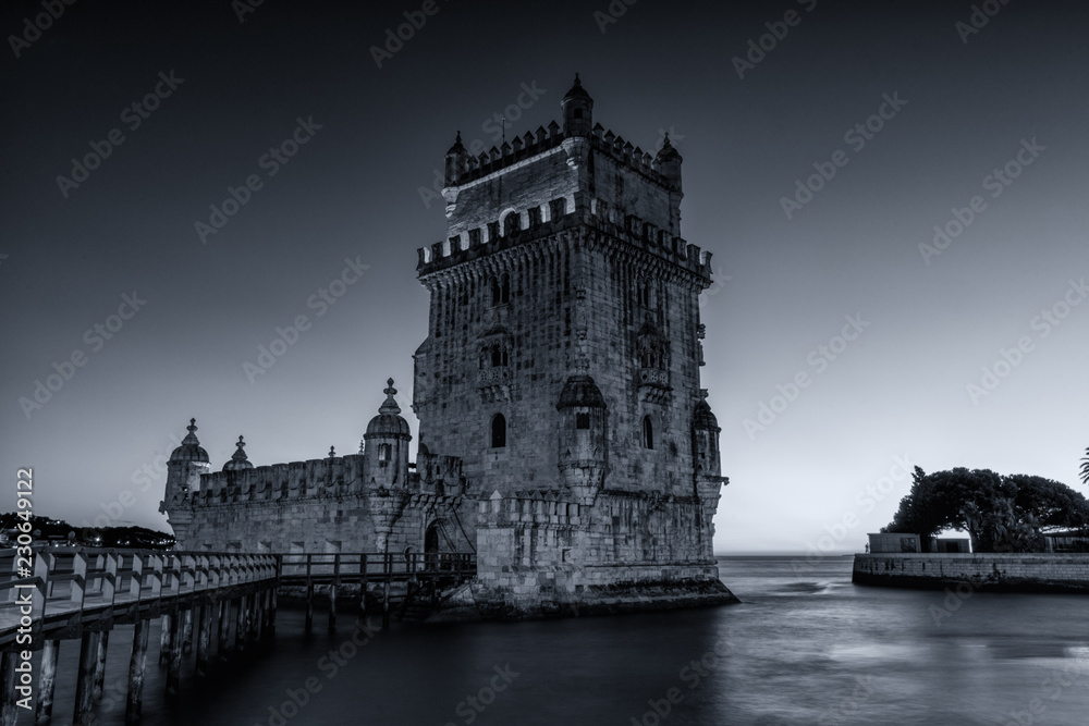 Black & white photograph of the  Belem Tower (Belém Tower) at sunset.  A medieval castle fortification on the Tagus river of Lisbon Portugal