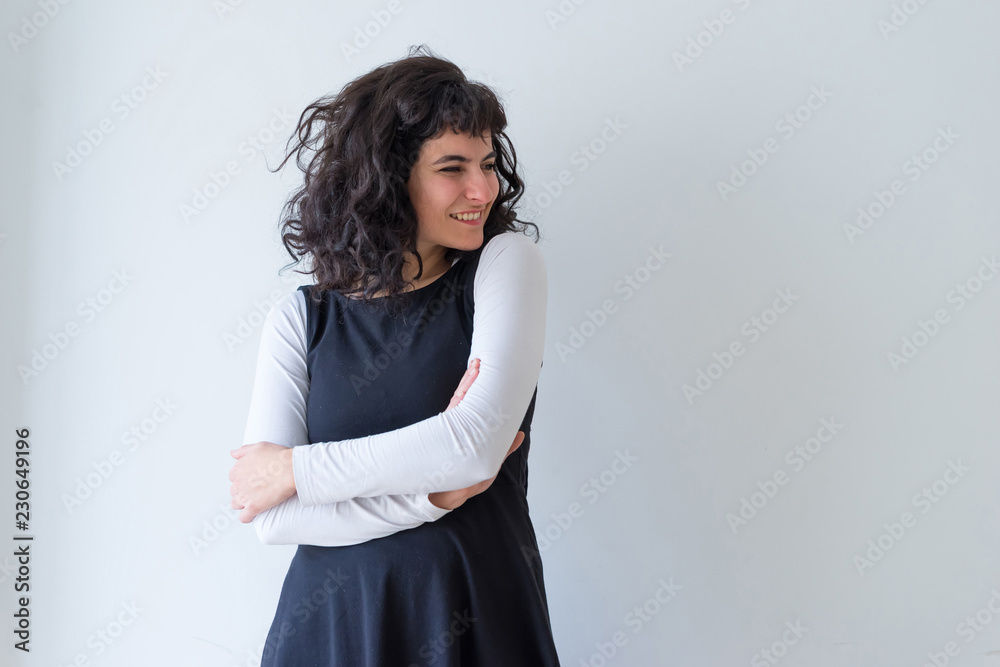 Fototapeta premium Portrait of a beautiful happy young woman in an elegant dress while standing in front of a white wall.