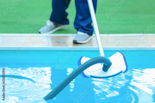 Male worker cleaning outdoor pool with underwater vacuum