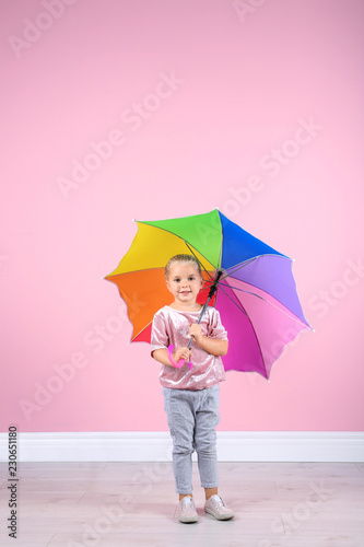 Little girl with rainbow umbrella near color wall. Space for text