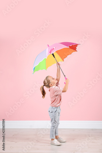 Little girl with rainbow umbrella near color wall