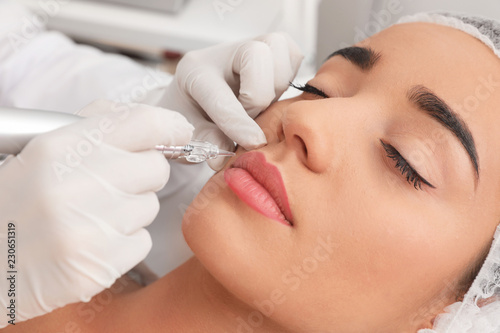 Young woman undergoing procedure of permanent lip makeup in tattoo salon, closeup