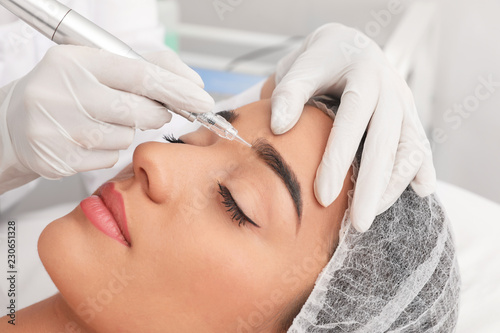 Young woman undergoing procedure of permanent eyebrow makeup in tattoo salon, closeup