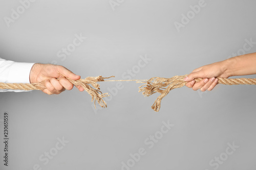 Man and woman pulling frayed rope at breaking point on gray background