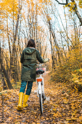 rear view of woman carrying bicycle in yellow autumnal forest