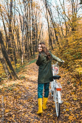 Cheerful woman carrying bicycle in yellow autumnal forest