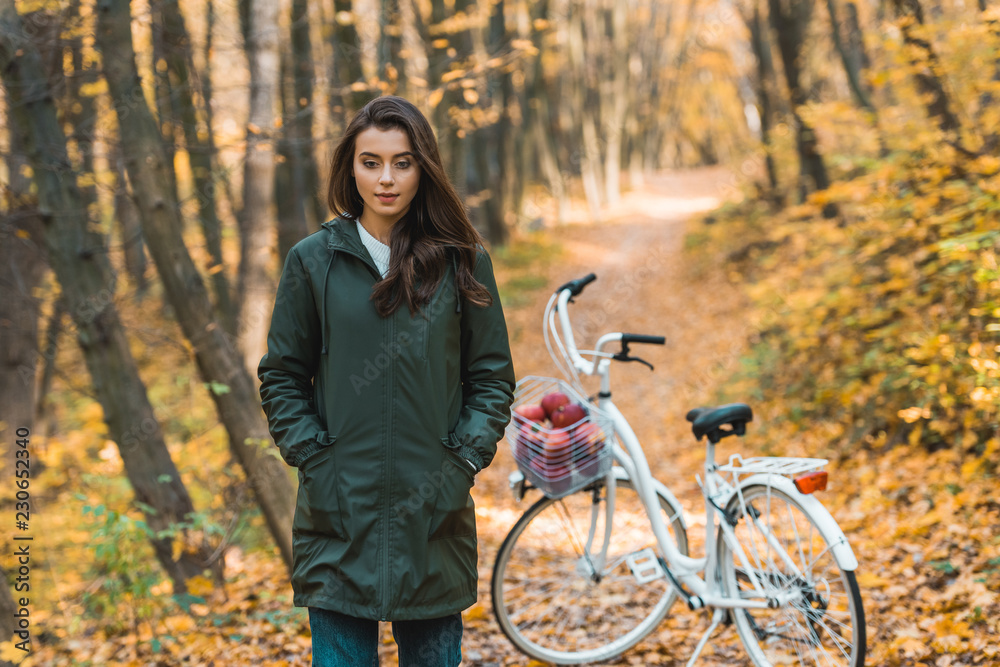Fototapeta premium beautiful young woman walking near bicycle in autumnal forest