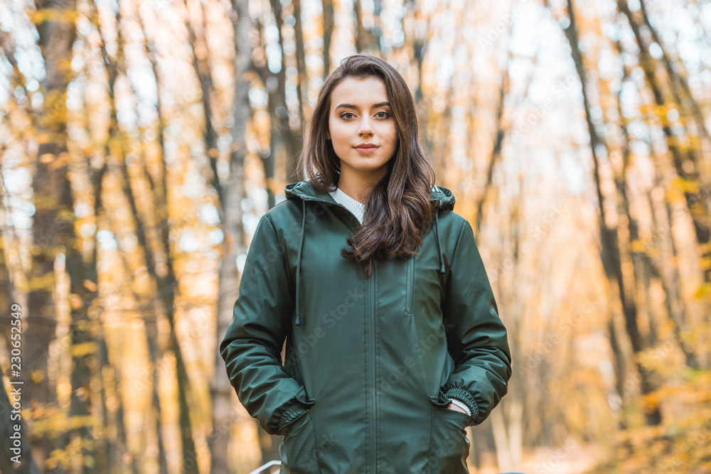 Beautiful young woman in jacket looking at camera in autumnal forest Beautiful young woman in jacket looking at camera in autumnal forest