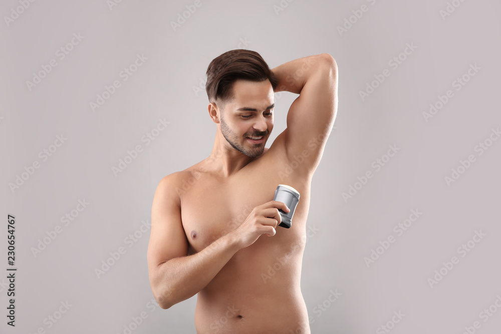 Obraz premium Young man using deodorant on gray background