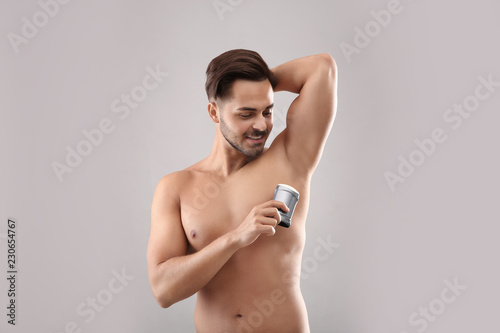 Young man using deodorant on gray background