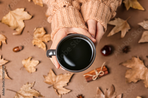 Woman in autumn sweater holding cup of hot cozy drink over color background, top view
