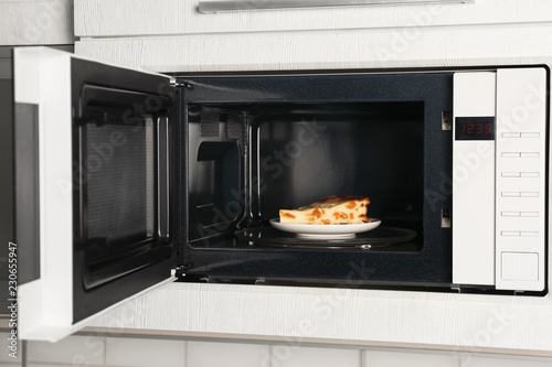 Open modern microwave oven with dessert in kitchen